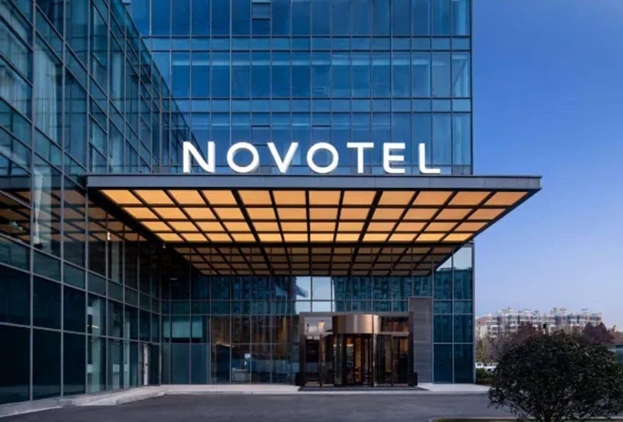 Een moderne hotelentree met een glazen gevel en een bord waarop 'NOVOTEL' staat.