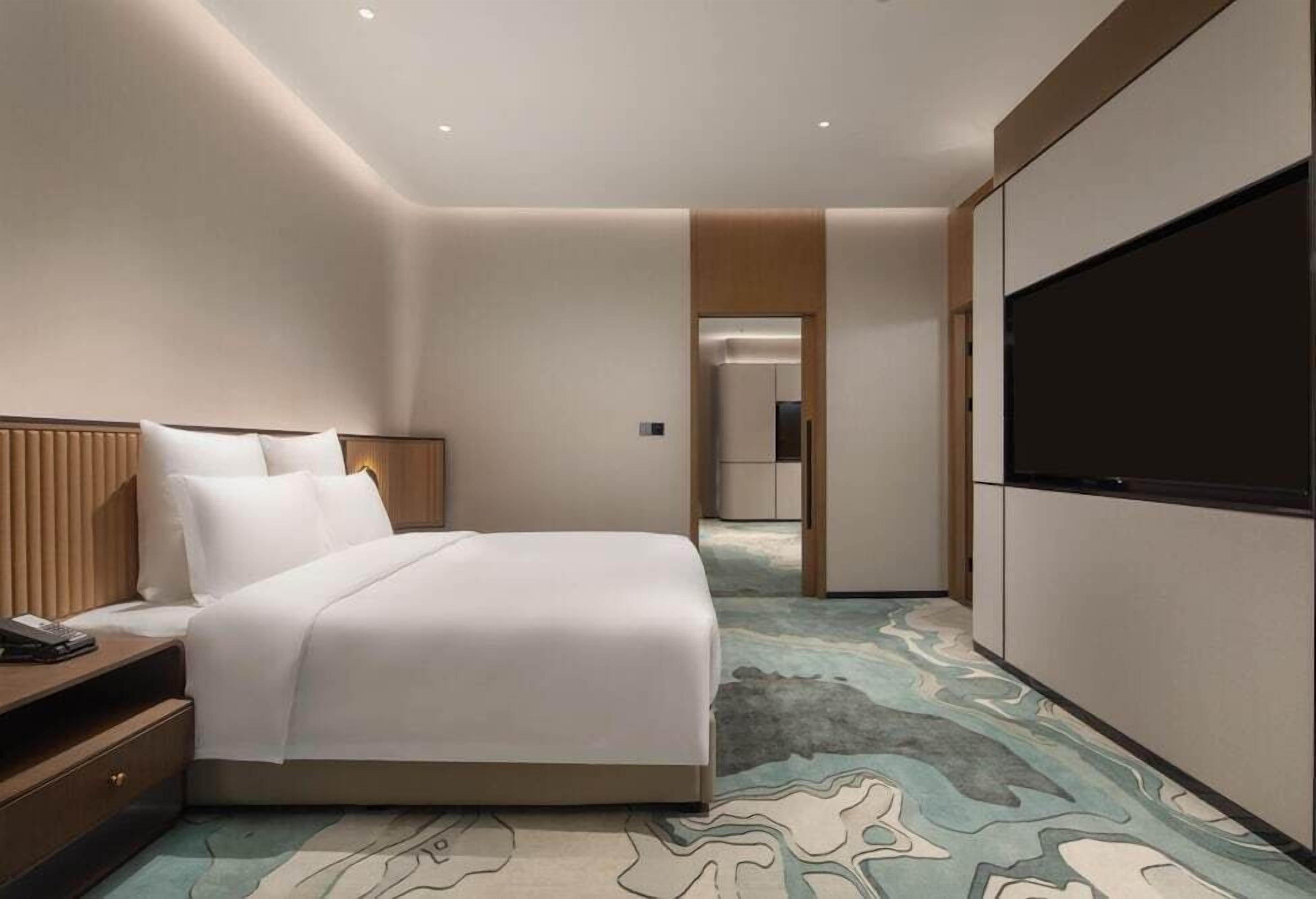 Ein modernes Hotelzimmer mit Bett, Nachttisch und großem Fernsehbildschirm.