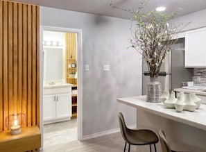 A modern kitchen with white cabinets, a wooden accent wall, and a vase with branches. - Your Montrose Studios Sleeps 80/40BR/40BA/30PA (Houston)