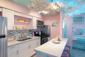 Cocina moderna con armarios blancos, un refrigerador de acero inoxidable, microondas y estufa. Hay una barra con taburetes y un pastel decorativo en la encimera.