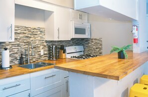 A modern kitchen with white cabinets, a microwave, a gas stove, a sink, and a wooden countertop. - Your Montrose Studios Sleeps 80/40BR/40BA/30PA (Houston)