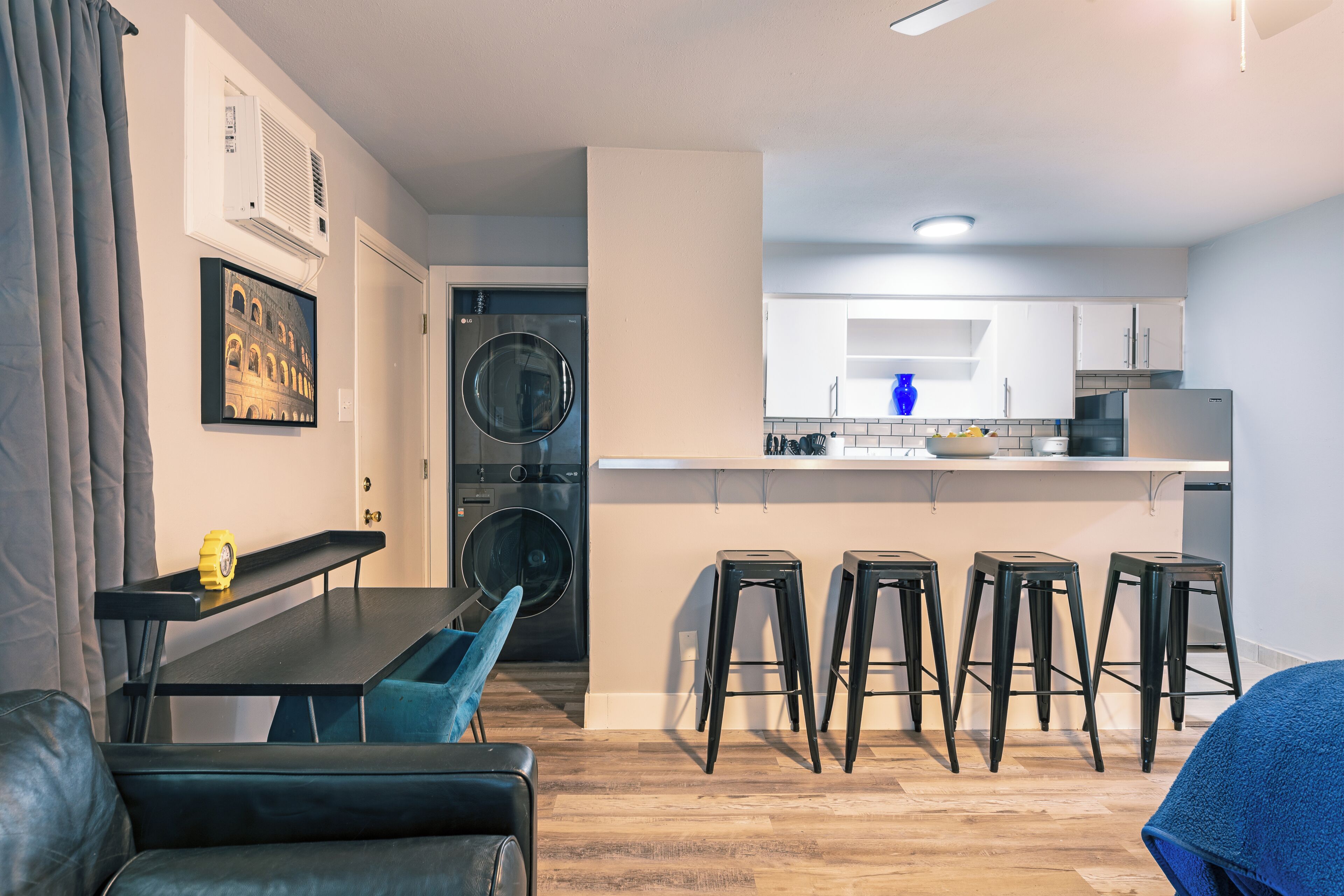 A compact living space with a kitchenette, a washing machine, and a dining area with bar stools.