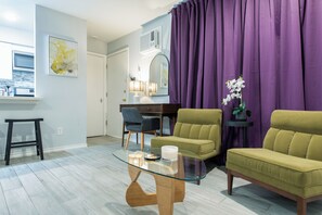 A living room with a glass coffee table, two green sofas, a small side table with a plant, and a purple curtain. - Your Montrose Studios Sleeps 80/40BR/40BA/30PA (Houston)
