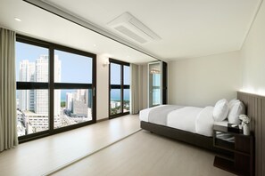 A modern hotel room with a large bed, a nightstand, and a view of the cityscape through floor-to-ceiling windows. - The Hotel Sokcho (Sokcho)
