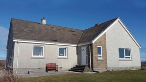 Une maison à deux étages avec un porche à l’avant, un banc et un ciel dégagé.