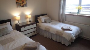 Une chambre avec deux lits, une table de chevet avec des lampes, un tableau au mur et une fenêtre donnant sur un beau paysage.
