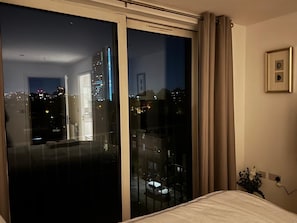 Ein Zimmer mit einer großen Schiebeglasdoor zur Terrasse, einem Bett mit weißer Bettdecke, einem gerahmten Bild an der Wand und einer Steckdose mit Kabel.
