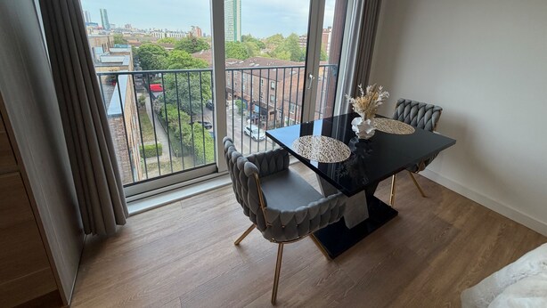 Un espace de salle à manger moderne avec une table et des chaises en verre, un pied de table noir et une vue sur le paysage urbain à travers de grandes fenêtres.