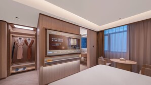 Ein Hotelzimmer mit einem großen Bett, einem Fernseher, einer Sitzecke und einem Kleiderschrank mit Bademänteln.