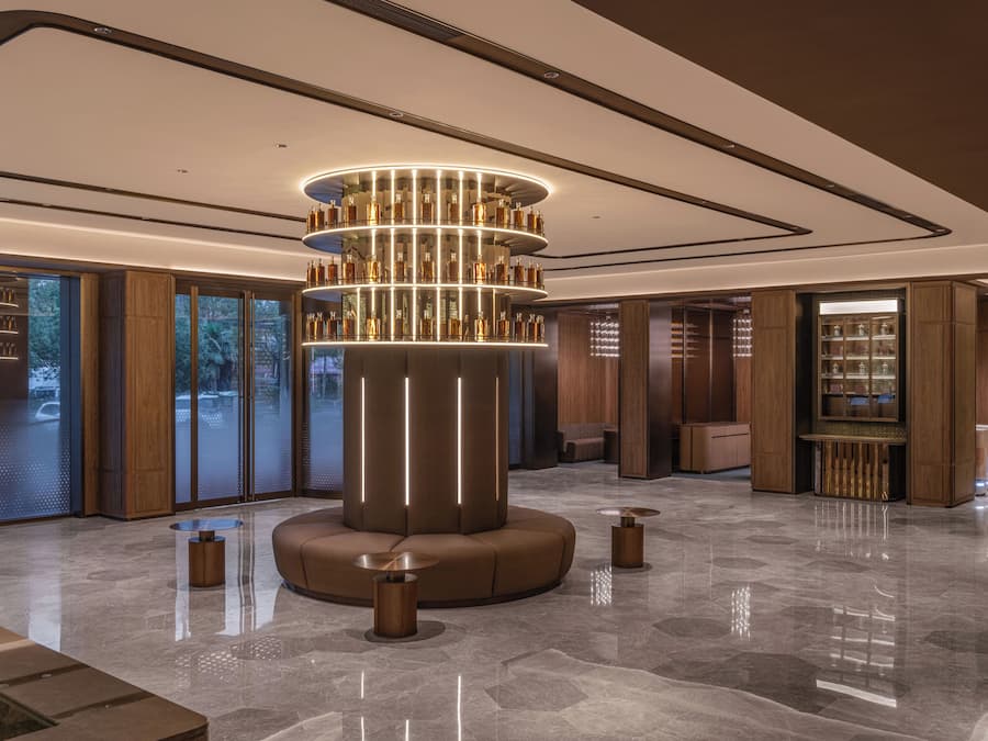 A modern lobby with a central cylindrical light fixture, wooden paneling, and a glass door leading outside.