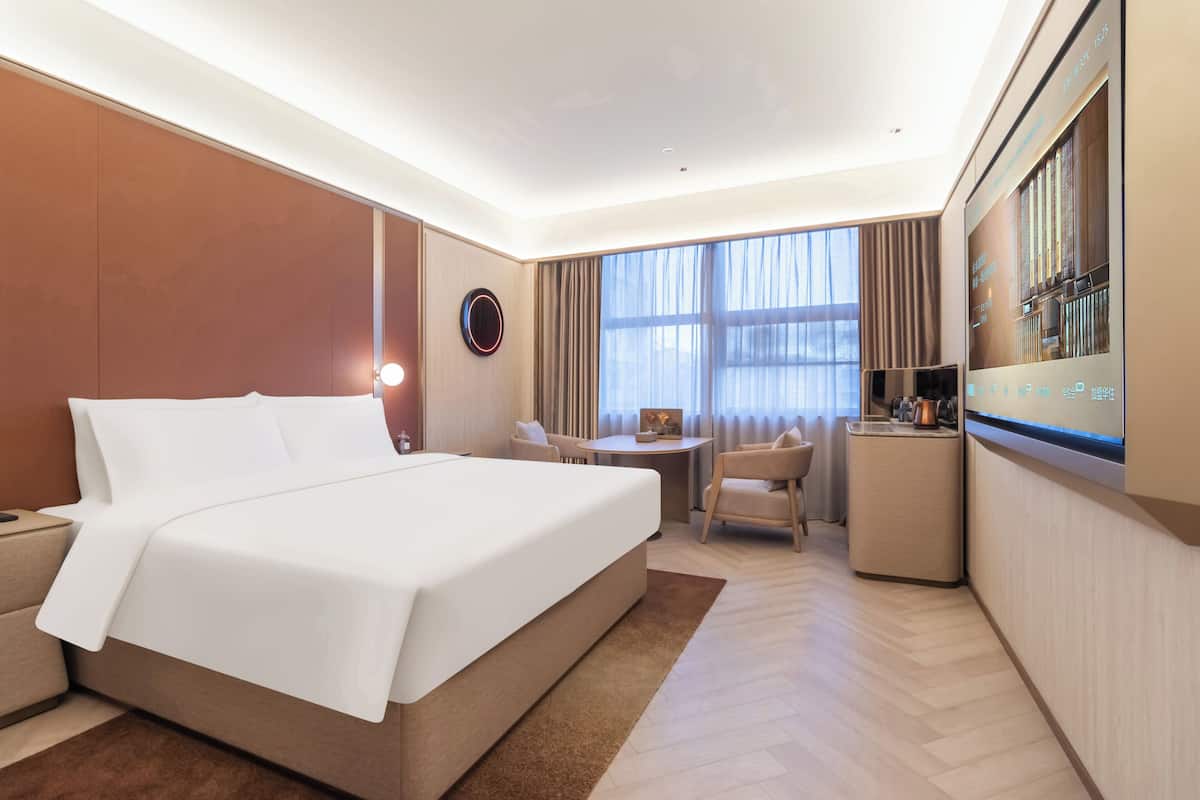 Een hotelkamer met een groot bed, een bureau, een stoel, een televisie en een raam met gordijnen.