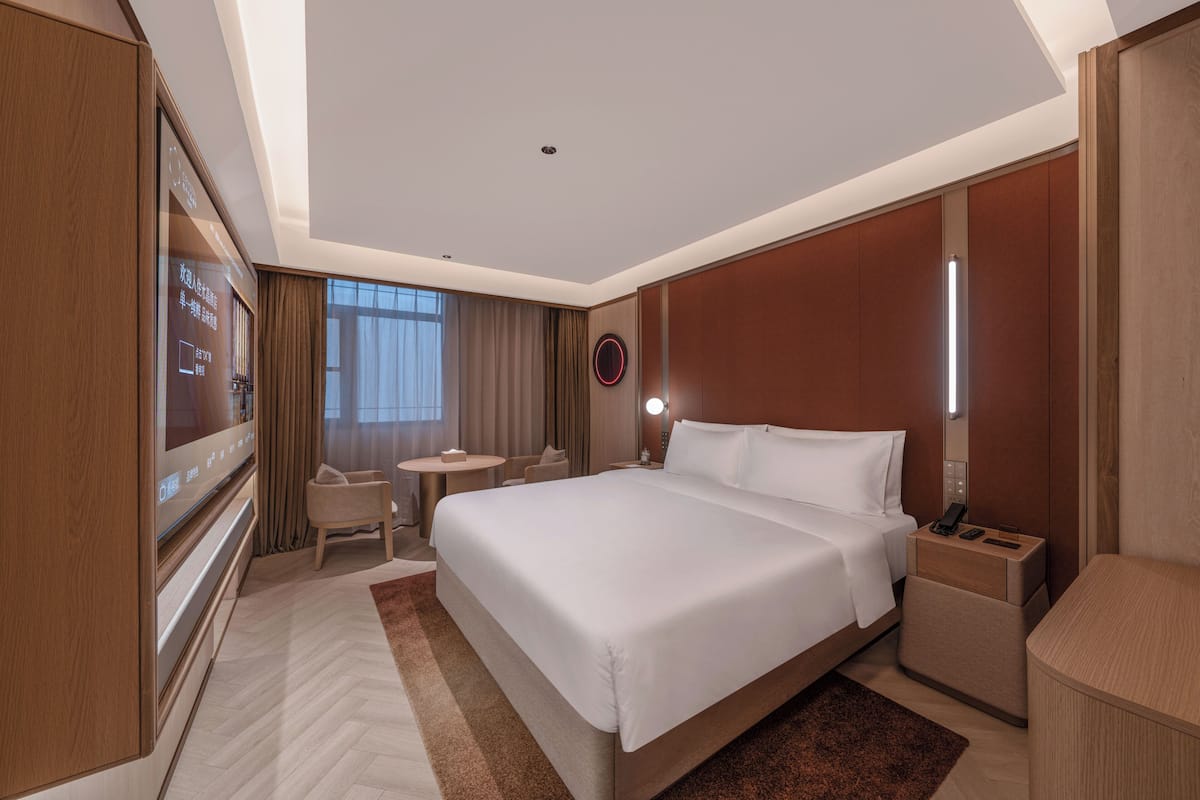 Een moderne hotelkamer met een groot bed, een televisie, een bureau en een ronde spiegel.