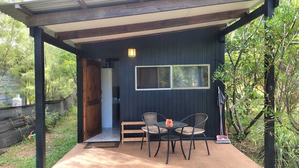 A covered outdoor seating area with a table and chairs, a window, and a door leading to the interior.