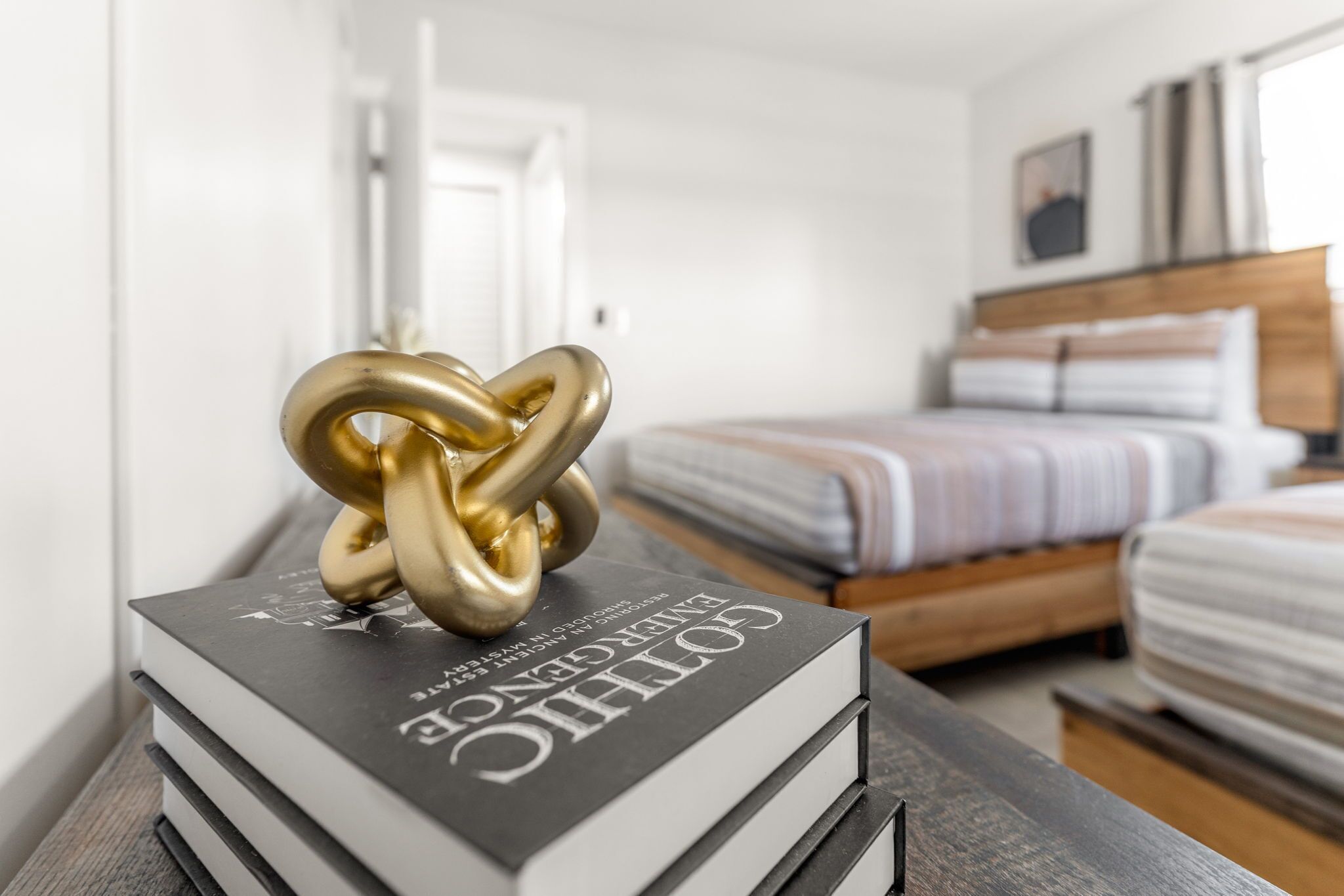 Una camera d'albergo con un letto, un comodino con un libro e una scultura dorata a nodo decorativo.