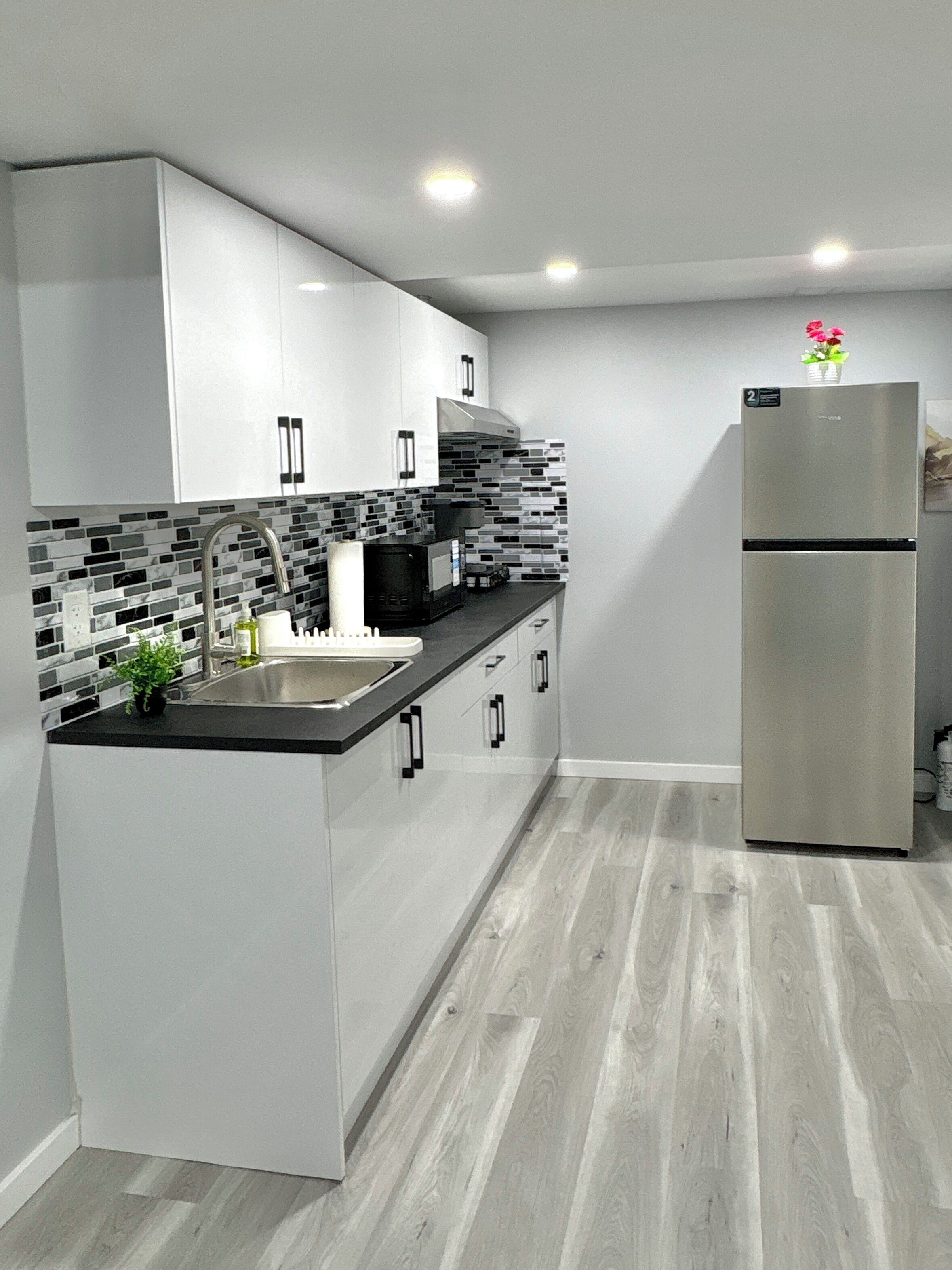 Una cucina moderna con mobili bianchi, un piano di lavoro nero, un frigorifero in acciaio inossidabile e uno schienale piastrellato.