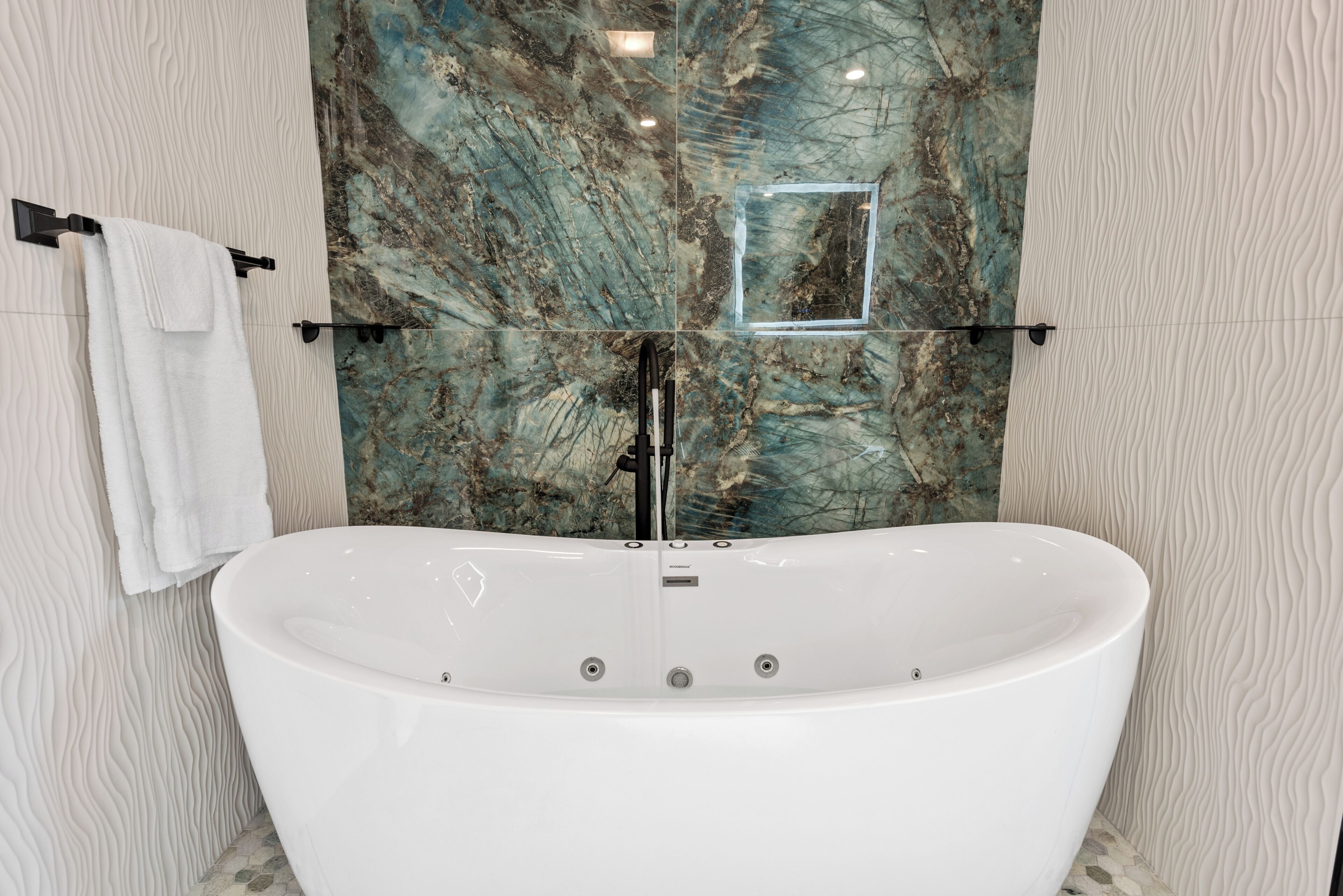 A freestanding bathtub in a bathroom with a marble backsplash and textured walls.