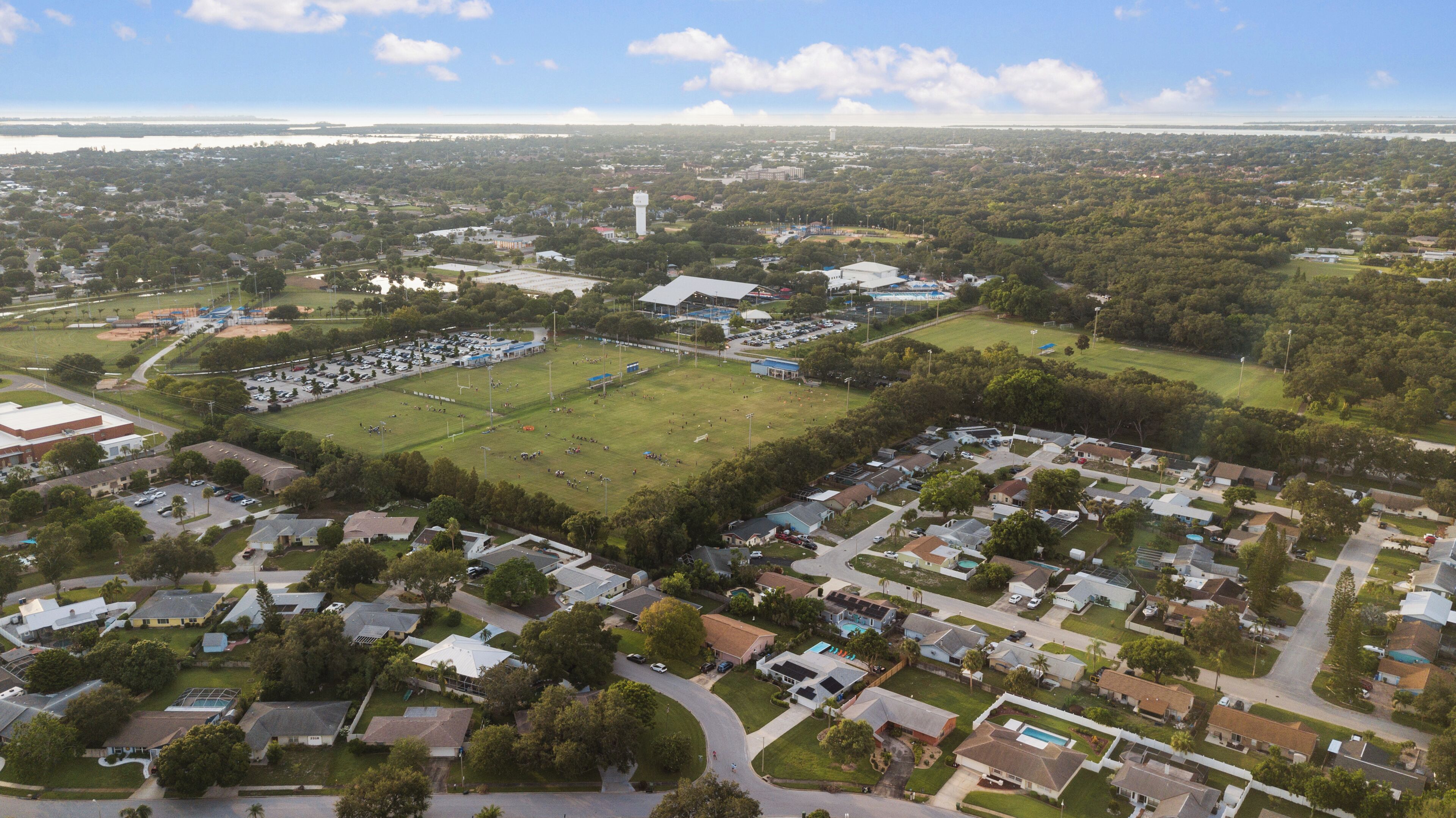 An aerial view of a residential area with houses, a large open field, and a sports field.