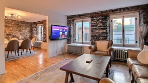 Ein Wohnzimmer mit Steinwand, Wandfernseher, Essbereich mit Stühlen und Kamin.