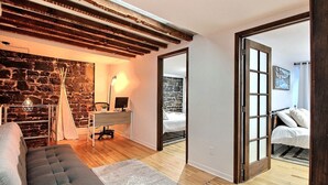 Ein Zimmer mit Steinwand, einem Schreibtisch mit Computer, einem Bett und Blick durch eine offene Tür.