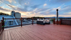 Eine Holzterrasse mit Gartenmöbeln, einem Metallgeländer und Blick auf die Stadt.