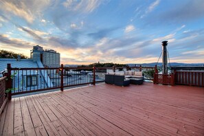 Eine Holzterrasse mit Gartenmöbeln, einem Metallgeländer und Blick auf die Stadt.