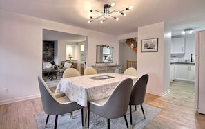 Ein Essbereich mit einem Marmortisch, grauen Stühlen, einer Chandelüster und einer Küche im Hintergrund.