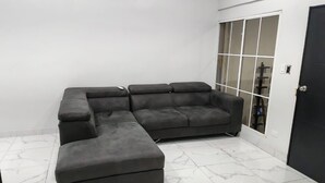 A sectional sofa in a room with white walls and a tiled floor. - House col. Ivu main street (Ahuachapán)
