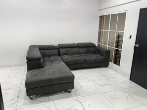 A sectional sofa in a room with white walls and a tiled floor. - House col. Ivu main street (Ahuachapán)