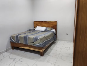 A single bed with a wooden headboard in a room with white marble flooring. - House col. Ivu main street (Ahuachapán)