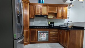 A kitchen with wooden cabinets, a stainless steel refrigerator, a stove, and a microwave. - House col. Ivu main street (Ahuachapán)