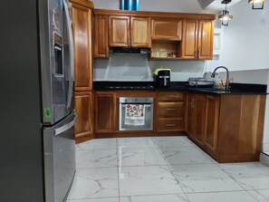 A kitchen with wooden cabinets, a stainless steel refrigerator, a stove, and a microwave. - House col. Ivu main street (Ahuachapán)