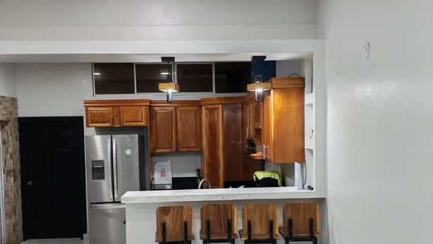 A modern kitchen with wooden cabinets, a stainless steel refrigerator, and a marble-tiled floor. - House col. Ivu main street (Ahuachapán)