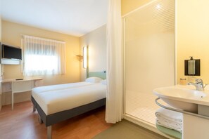 A hotel room with a bed, a desk, a TV, a bathroom with a sink and mirror, and a shower. - Ibis Budget Les Sables Olonne Sur Mer (Les Sables-d'Olonne)