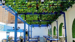 Ein Straßencafé mit Tischen, Stühlen und einem blauen Geländer, darüber sprießt Grün.