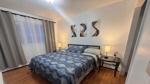 A bedroom with a bed, two bedside tables with lamps, a window with curtains, and abstract wall art. - Central Fairbanks 3BR/2BA,  King Bed,  Sleeps 6, Free Laundry (Fairbanks)