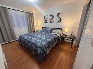 A bedroom with a bed, two bedside tables with lamps, a window with curtains, and abstract wall art. - Central Fairbanks 3BR/2BA,  King Bed,  Sleeps 6, Free Laundry (Fairbanks)