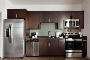 A modern kitchen with stainless steel appliances, dark wood cabinets, and a tiled backsplash. - Sports Illustrated Resorts Nashville Music Row (Nashville)