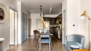 Una cocina moderna con armarios oscuros, un comedor con mesa y sillas, y una sala de estar con sofá y lámpara.