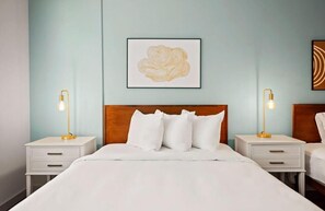 Ein Hotelzimmer mit einem Bett, zwei Nachttischen mit Lampen, einem hölzernen Kopfteil und einem gerahmten Kunstwerk an der Wand.