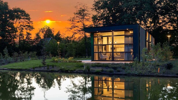 Ett modernt hus med stora fönster, en trädgård och en spegelbild i vattnet.