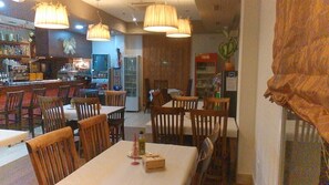 En restaurant med træborde og -stole, hængende lamper og et barområde med hylder fyldt med flasker.