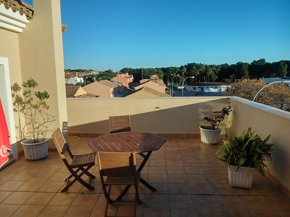 A balcony with a table and chairs, potted plants, and a view of buildings and trees. - Hotel Las Canteras de Puerto Real (Puerto Real)