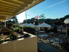 Eine Terrasse im Freien mit Tischen, Stühlen, Sonnenschirmen und Flaggen.