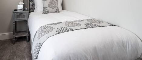 A neatly made bed with a patterned bedspread, a bedside table with a lamp, and a small nightstand.