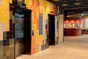 An elevator with a colorful tile wall, a sign indicating 'Trio 14', and a bar area in the background. - Dein Apart (Unterfoehring)