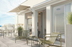 Un área de estar exterior moderna con sillas de metal y una mesa, una planta en maceta y vista al mar.