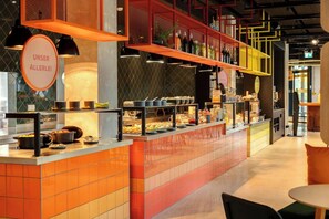 A buffet area with a variety of food options, a sign reading 'UNSER ALLERLEI', and a modern interior design with orange and yellow accents. - Dein Apart (Unterfoehring)