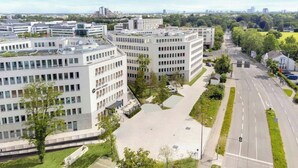 A modern building complex with multiple office buildings, a parking area, and a road with greenery on the sides. - Dein Apart (Unterfoehring)