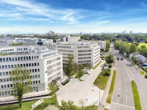 A modern building complex with multiple office buildings, a parking area, and a road with greenery on the sides. - Dein Apart (Unterfoehring)