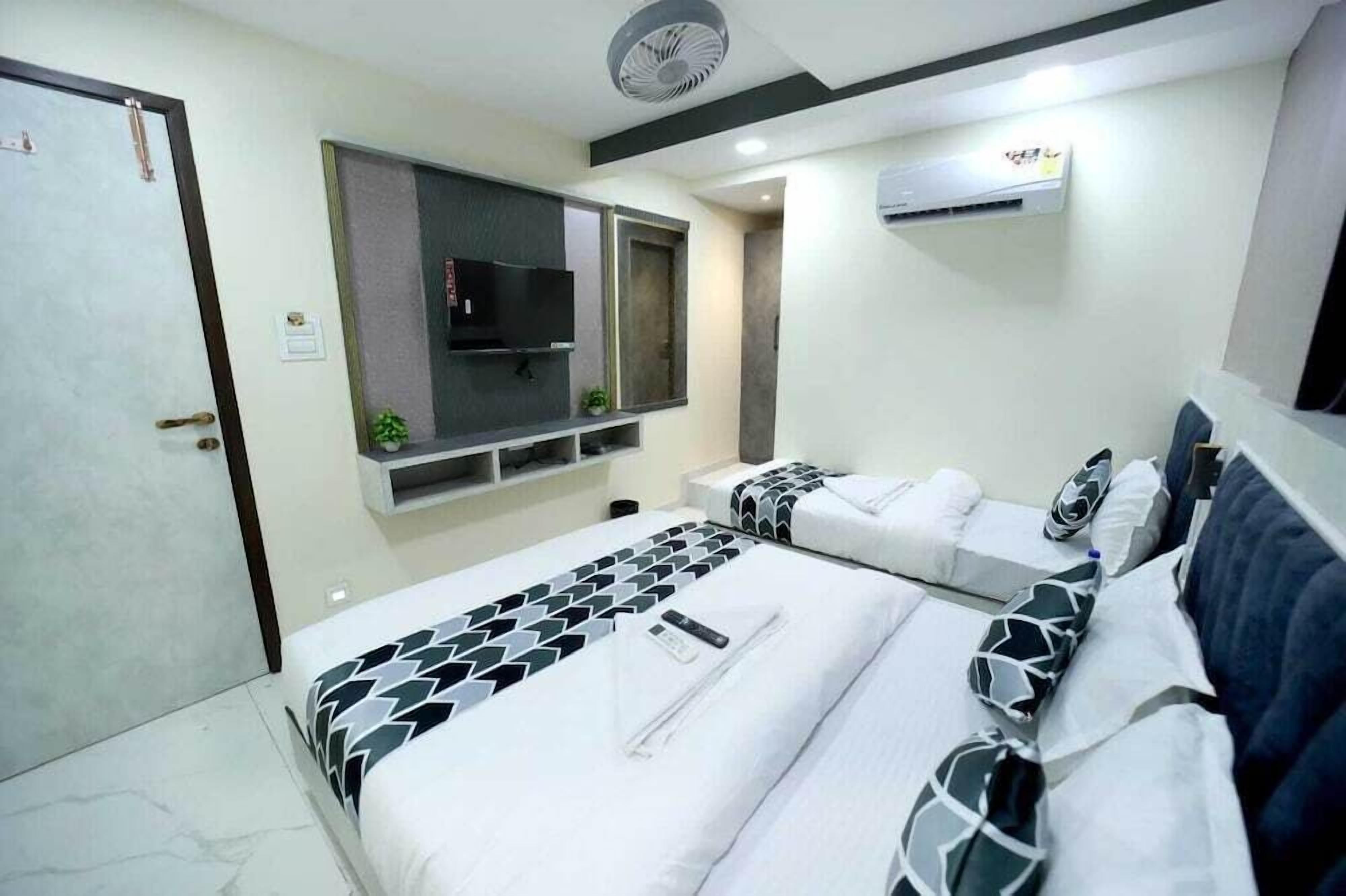 A hotel room with a bed, a TV, a wall-mounted air conditioner, and a door.